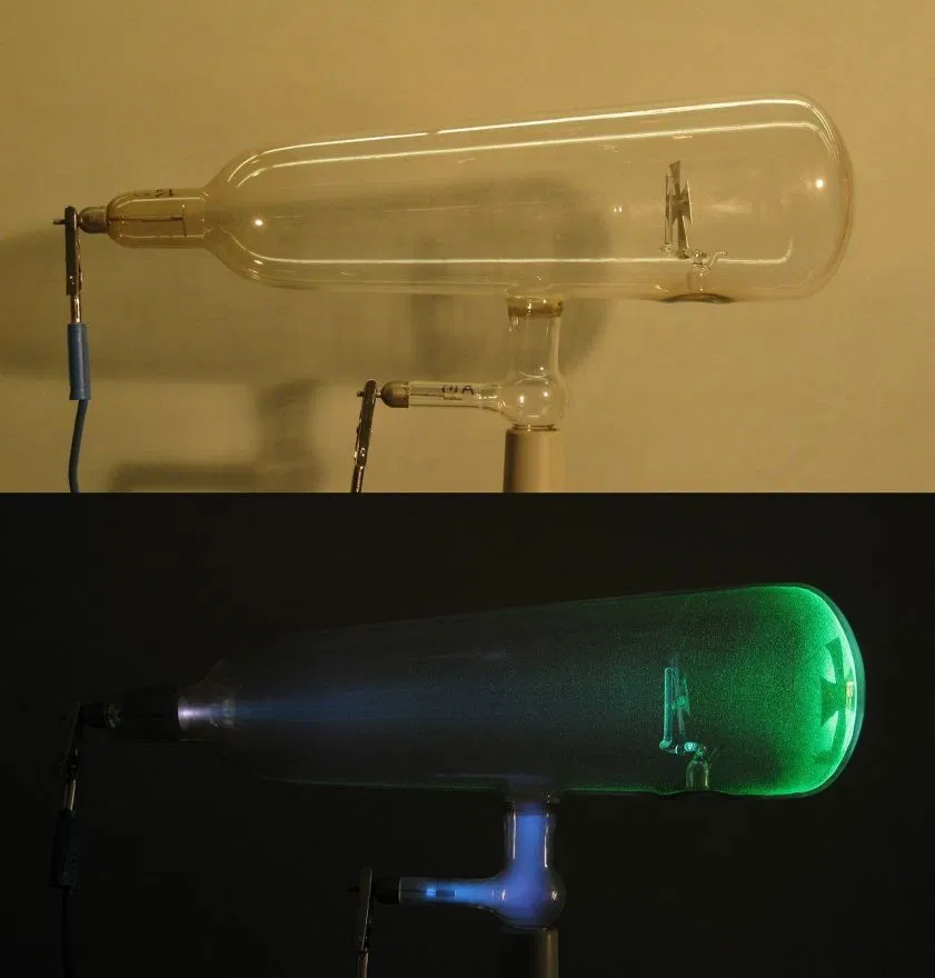 Two views of a Crookes tube, glowing green as current passes through it.