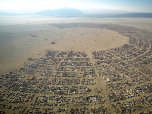 Aerial photograph of Black Rock City, the temporary Burning Man settlement: a huge semicircular grid of camps and roads on a flat Nevada desert, with mountains behind